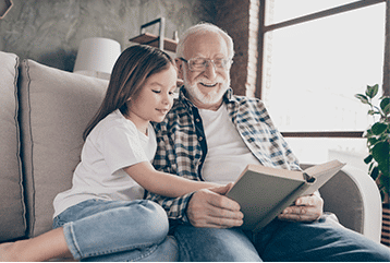 An older man struggling with hearing loss still tries to read a book to his granddaughter in Iowa.